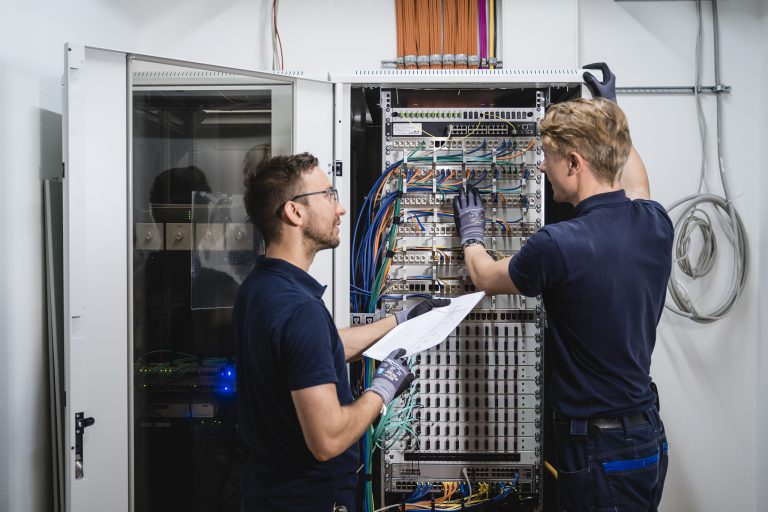 Zwei Techniker vor einem Serverschrank mit TRIAX und GSS Kopfstationen.